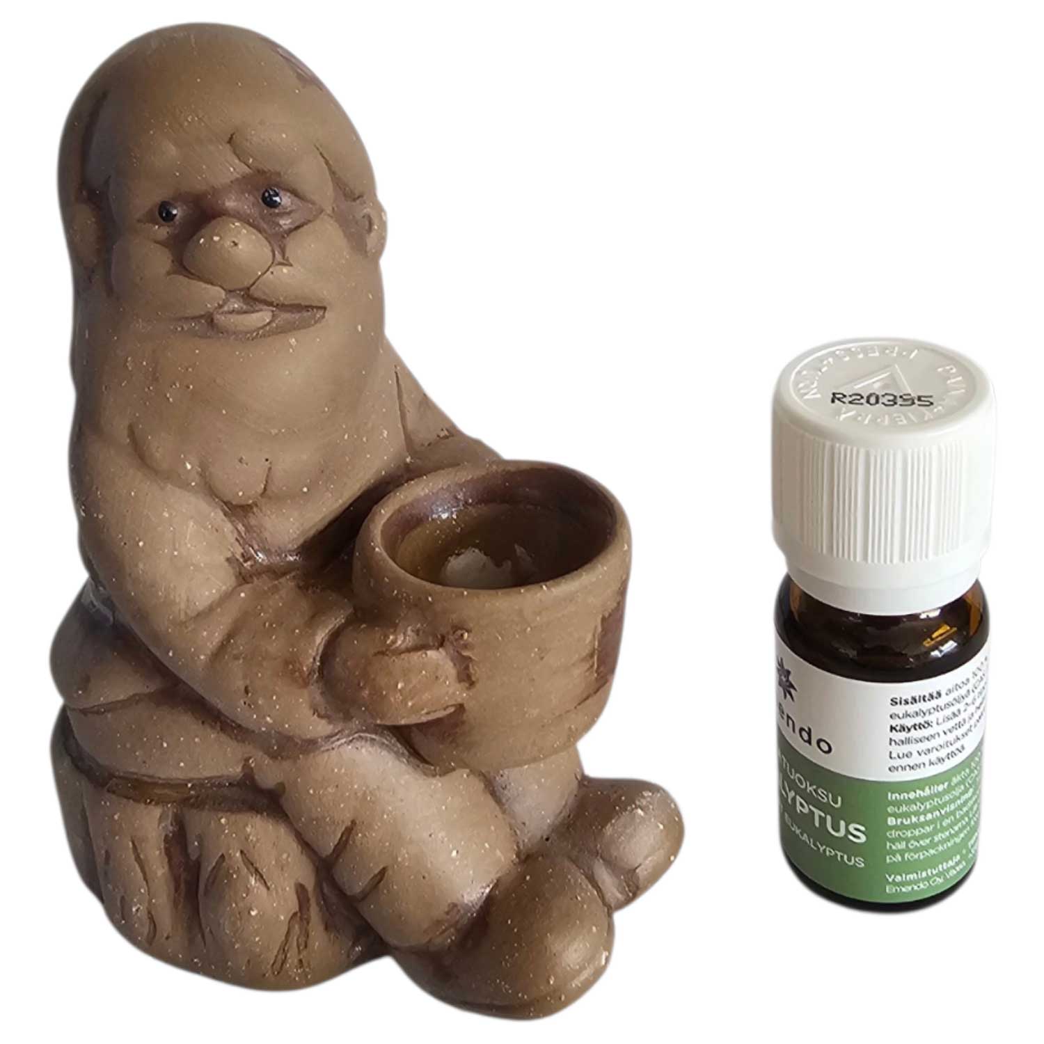Eine Keramikzwergfigur mit einer kleinen Schüssel neben einer kleinen Flasche ätherischem Öl.