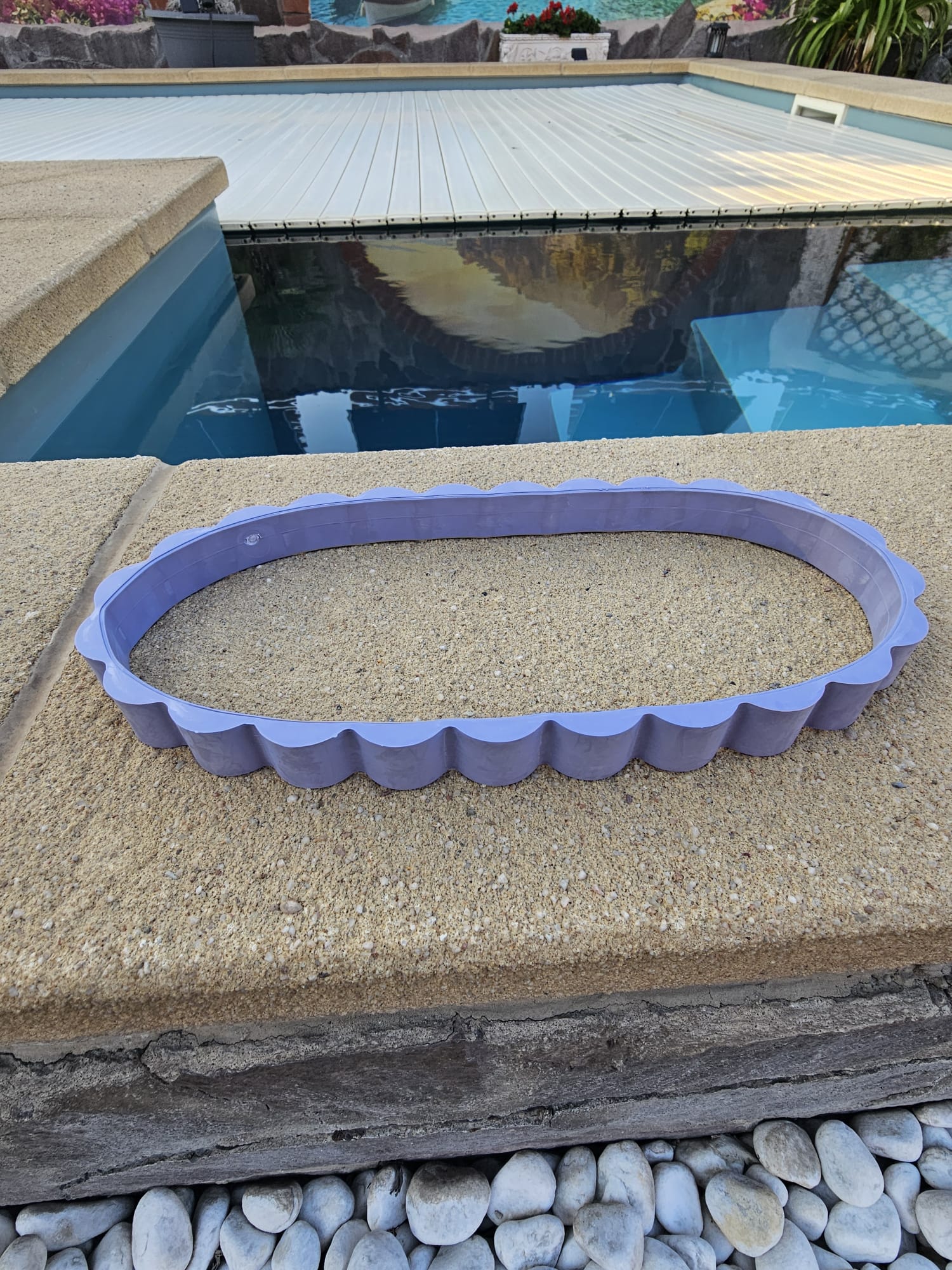 Eine ovale, hellviolette Beckenrandverkleidung aus Kunststoff, die auf einer steinernen Beckenumrandung platziert ist.