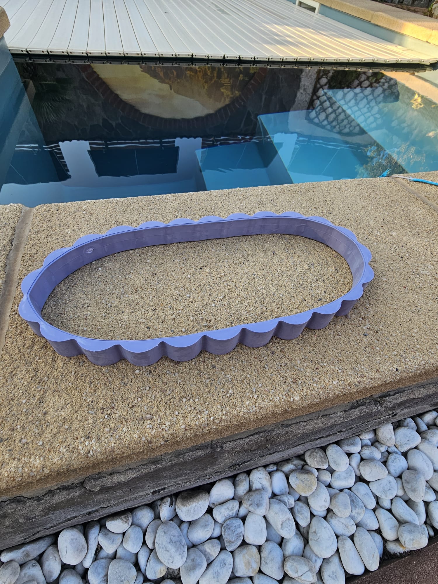 Ein ovaler, violetter Kantenschutz für die Poolabdeckung, der auf der Oberfläche des Pooldecks platziert ist.